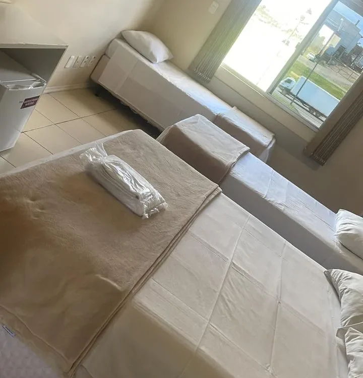 Dois sofás brancos em uma sala com piso de cerâmica, janela ampla com vista para exterior e climatizador na parede